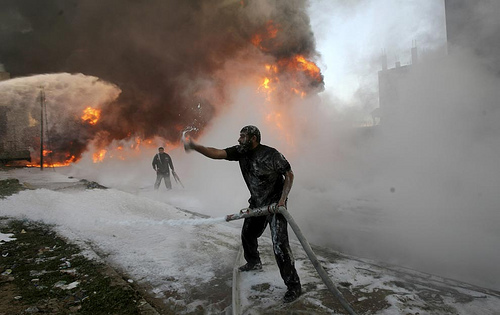 Palestinian firefighters try to extinguish flames at a medical warehouse after an Israeli airstrike (Photo by Amir Farshad Ebrahimi on flickr)
