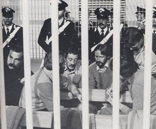 图片：1982年，因杀害阿尔多·莫罗而受审的红色旅成员，其中包括马里奥·莫雷蒂（左三）和普洛斯佩罗·加里纳利（戴眼镜），他们都出身于低微的工人阶级和农民阶级（加里纳利在共产党的青年时期就开始了他的政治活动）